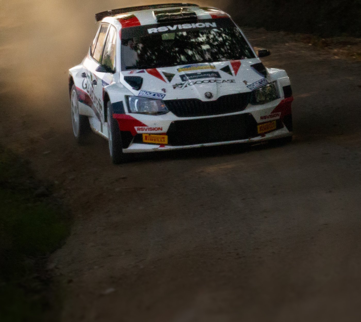 Auto da rally bianca in derapata su sterrato, con la polvere in controluce