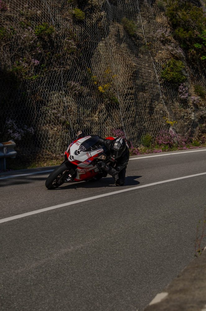 Moto rossa e bianca in piega lungo una parete di roccia